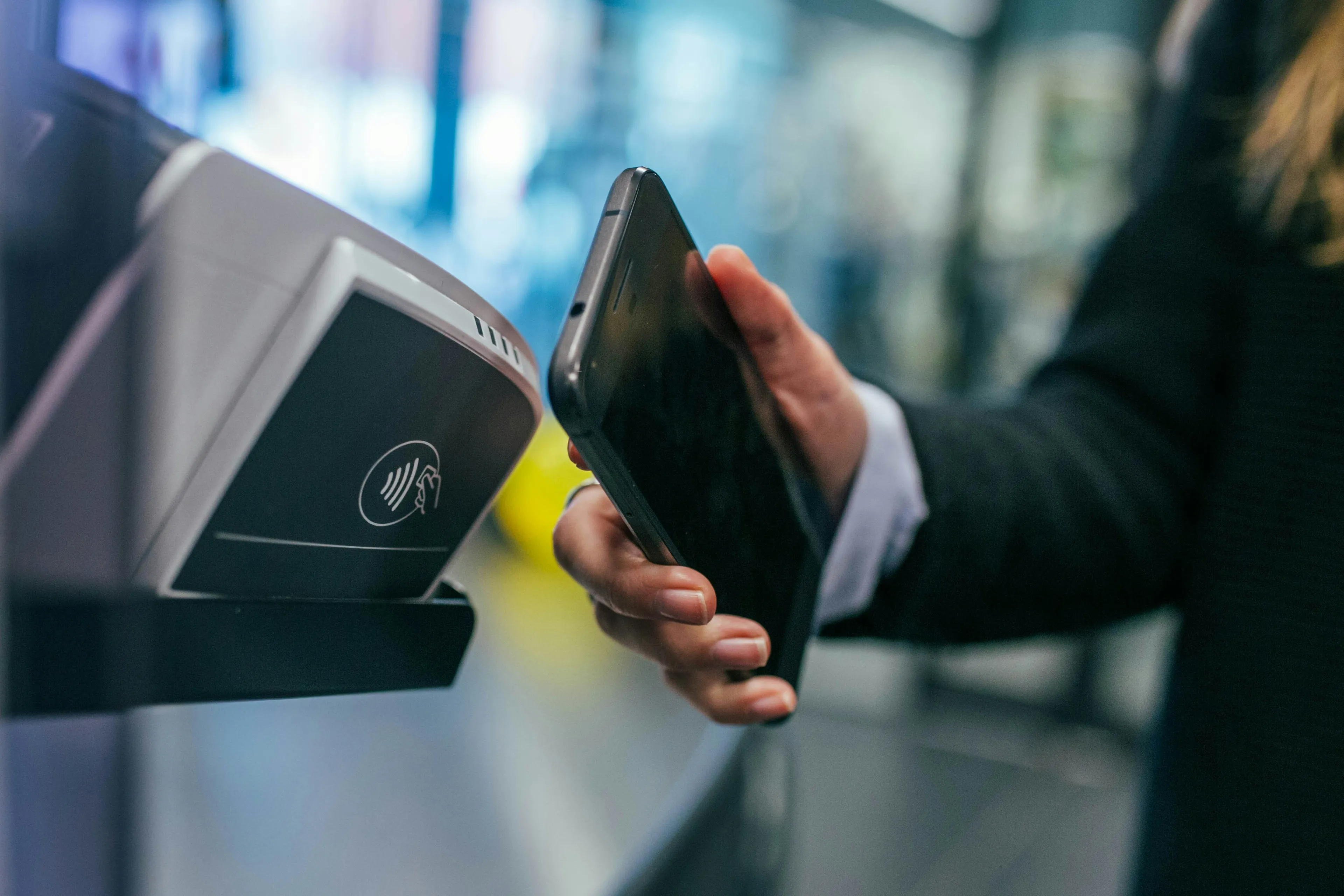 Nahaufnahme einer Hand, die ein Smartphone mit Apple Pay an das Kartenterminal eines Blumenautomaten hält, im Hintergrund unscharf ein beleuchtetes Fach mit Blumenstrauß, Abendstimmung