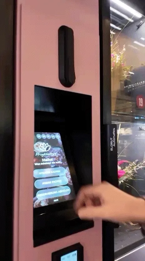 Kunde bedient den beleuchteten Touchscreen eines Blumenautomaten und wählt einen Strauß aus